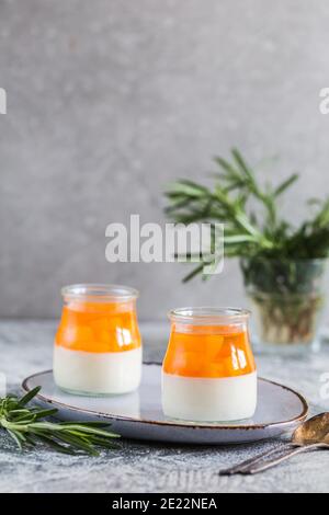 Hausgemachte Panna Cotta mit Scheiben von Pfirsich und Pfirsich Gelee in Glasgefäßen auf einem grauen Beton Hintergrund. Stockfoto