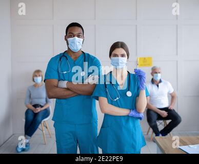 Männliche und weibliche Ärzte tragen Uniformen und Gesichtsmasken, halten Spritze mit Coronavirus-Impfstoff in der Klinik Stockfoto