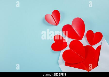 Envolope und Rote Papierherzen isoliert auf blauem Hintergrund. Flach liegend, Draufsicht, Kopierbereich. Valentinstag-Konzept. Stockfoto