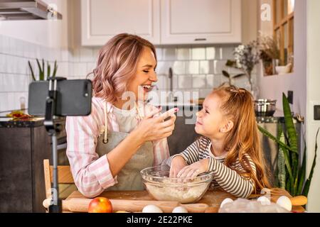 Food Bloggerinnen Mutter und Tochter kneten Teig und lächeln beim Backen, in der hellen Küche zu Hause Stockfoto