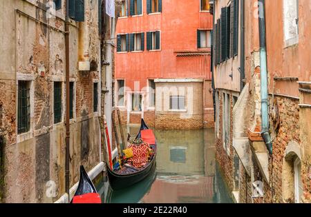 Ruhige Wasserallgasse - EINE farbenfrohe und dekorative venezianische Gondel, ein beliebtes Touristenruderboot, im Leerlauf in einer engen Wasserstraße in Venedig, Venetien, Italien. Stockfoto