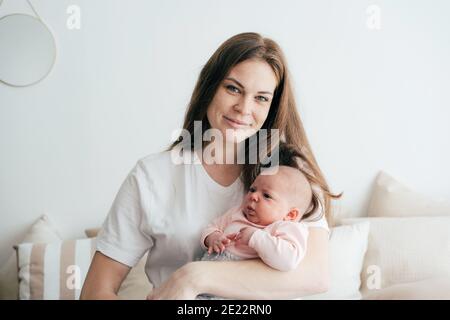 Schöne junge Rotschopf Sommersprossen Mutter hält und umarmt ein neugeborenes Monat altes Baby. Zarte Mutterschaft und Geburtsglück. Eine Familie. Stockfoto
