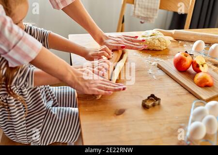Mama helfen Kind Tochter Rollen Teig für hausgemachte Kekse oder Kuchen. Zwei weibliche Generationen Familie genießen Kochprozess zusammen in der Küche, in Stockfoto