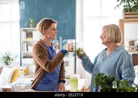 Ältere Frau mit Pflegekraft oder Pflegekraft in Innenräumen, trinken gesunden Smoothie. Stockfoto