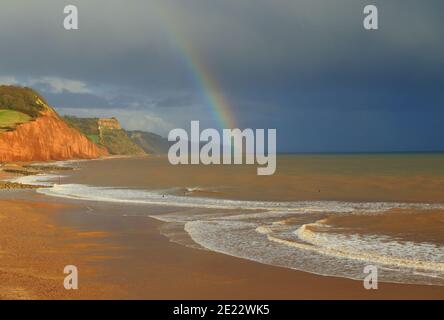 Regenbogen über Sandstrand in Sidmouth, Devon an der Jurassic Coast Stockfoto