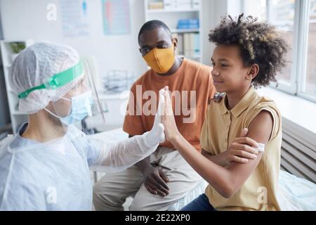 Seitenansicht Porträt eines lächelnden afroamerikanischen Jungen hoch fünf Krankenschwester nach covid Impfung in Klinik oder Krankenhaus, kopieren Raum Stockfoto