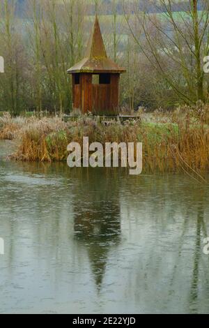 Hölzerne Vogelbeobachtungsversteck reflektiert auf dem See in Devon, Großbritannien Stockfoto