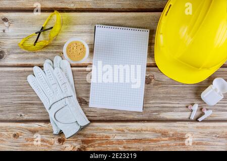 Bürobau Architekt Ingenieur arbeiten auf Spiral Notizblock auf gelben Schutzhelm auf Holzhintergrund. Stockfoto