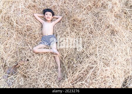 Porträt eines niedlichen kleinen asiatischen Jungen lächelnd und liegend auf Heu, Reisstroh. Stockfoto