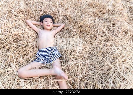 Porträt eines niedlichen kleinen asiatischen Jungen lächelnd und liegend auf Heu, Reisstroh. Stockfoto