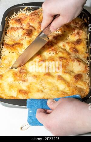 Schneiden Sie mit einem Messer in Portionen gekochter Lasagne. Lasagne zu Hause machen. Stockfoto