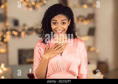 Überrascht afroamerikanische Frau in Kleid berühren Brust und lächeln Stockfoto