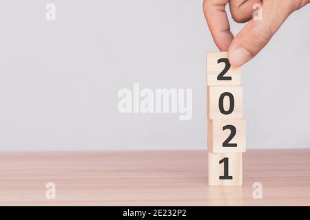Hand hält Holzklötze mit den Nummern 2021 und legt in einer Reihe den Anfang des neuen Jahres auf den Tisch. Frohes neues Jahr und Urlaubskonzept. Stockfoto