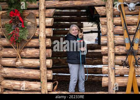 Ältere ältere Frau hält einen yorkshire Terrier Hund im Stehen In einer dekorierten Blockhütte Stockfoto