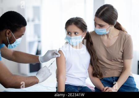 Mutter und Tochter in medizinischen Masken gegen covid-19 geimpft, Arzt Injektion von Coronavirus-Impfstoff Stockfoto