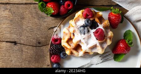 Hausgemachte Süßigkeiten mit Beeren. Draufsicht. Belgische Waffeln Erdbeeren, Blaubeeren auf Teller mit Leinwand auf altem Holzhintergrund. Frühstück auf rustikalen KI Stockfoto