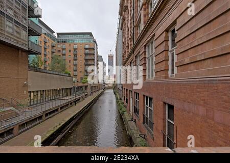 Alte Lagerhäuser und Wohngebäude entlang eines schmalen Kanals in Manchester, Vereinigtes Königreich. Weitwinkelansicht Stockfoto