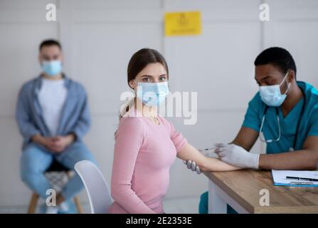 Schwarzer männlicher Arzt, der jungen Frau intramuskuläre Injektion verabreichten Arztpraxis Stockfoto