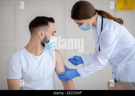 Impfung gegen covid-19. Ärztin injiziert Coronavirus-Impfstoff an den Arm des männlichen Patienten im Gesundheitszentrum Stockfoto