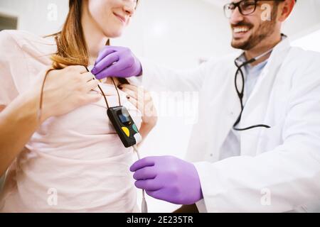 Junge fröhliche Arzt setzen Holter Monitor Gerät auf Mädchen Truhen. Stockfoto