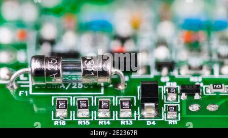 Elektrische Glasrohr Sicherung oder Widerstände, Diode und Transistor auf Leiterplatte im künstlerischen Detail. Kleine Sicherheitsvorrichtung auf grüne Leiterplatte gelötet. Stockfoto