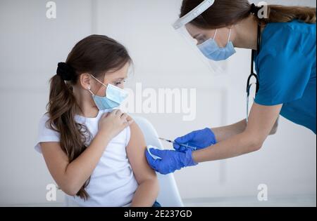 Covid-19-Impfung. Kleines Mädchen in Schutzmaske erhalten Coronavirus-Impfstoff-Injektion vom Arzt in der Klinik Stockfoto