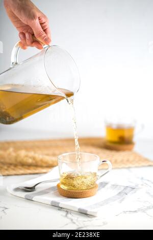 Eine Tasse Grüner Tee, der aus der Teekanne gießt Der weiße Hintergrund mit gelben Details Stockfoto