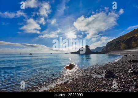 Bild von Bouley Bay an einem sonnigen Morgen mit blauem Himmel, Kiesstrand und kleine Insel mit Bäumen, ruhiges Meer mit kleinen Wellen Jersey Channel Islands Stockfoto