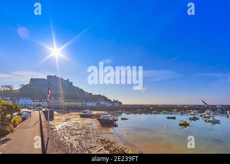 Bild von Gorey Harbour mit Angeln und Vergnügungsbooten, der Pier, Bullworks und Gorey Castle im Hintergrund mit blauem Himmel und der Sonne. Jersey, Stockfoto