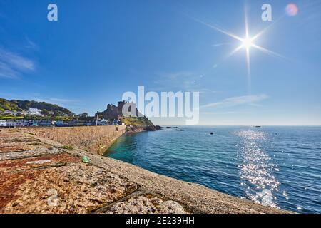 Bild von der Rückseite der Pier von Gorey Harbor mit Gorey Castle im Hintergrund mit einer Muschel Meer, Sonnenschein mit einem blauen Himmel am frühen Morgen genommen. Jers Stockfoto