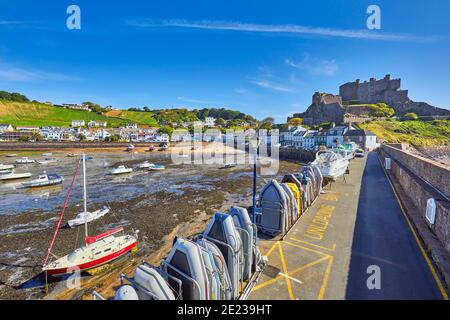 Bild von Gorey Harbour bei Ebbe mit geerdeten Booten, der Pier Bullworks und Gorey Castle im Hintergrund mit blauem Himmel. Jersey, Kanalinseln, Stockfoto