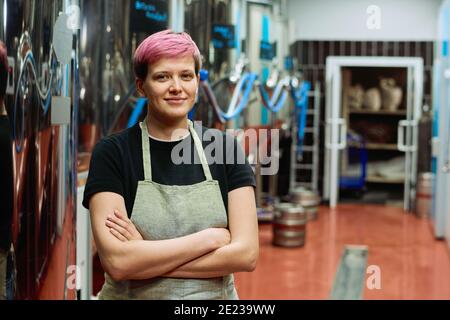 Junge erfolgreiche Arbeiterin der Bierfabrik im Vorfeld Überkreuzte Arme an der Brust, während sie vor der Kamera stehen Und lächelnd Stockfoto