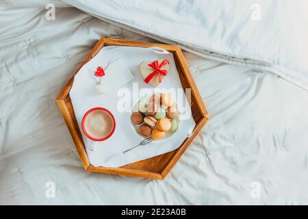 Draufsicht hausgemachtes Valentinstag-Frühstück im Bett für Liebhaber. Eine Tasse Kaffee, Makronen, herzförmige Geschenkbox mit rotem Band und leere Karte für wi Stockfoto