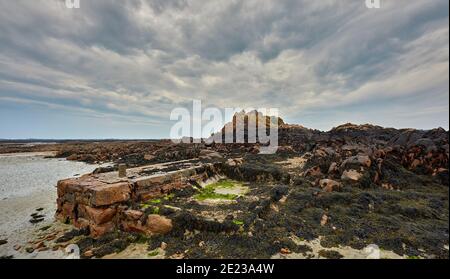 Der Strand bei Ebbe mit Felsen, Algen, kleinen Steinpier und einem bewölkten Himmel in Le Hocq, St Clements, Jersey Channel Islands. Stockfoto