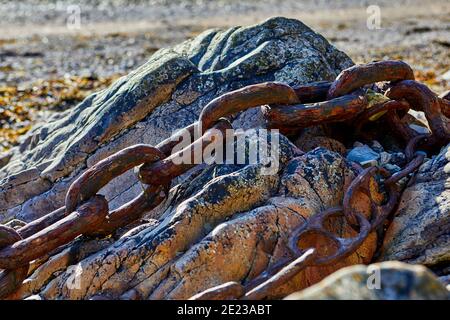 Abstraktes Bild von alten rostigen Ketten über einem Granitfelsen am Strand mit einer geringen Schärfentiefe, selektiver Fokus. Stockfoto