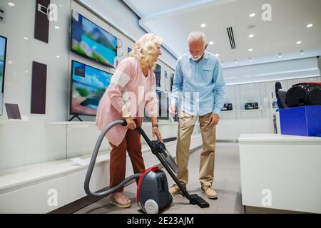 Glückliches Ehepaar, das einen neuen Staubsauger ausprobiert hat. Inneneinrichtung des Technikladens. Stockfoto
