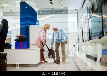 Glückliches Ehepaar, das einen neuen Staubsauger ausprobiert hat. Inneneinrichtung des Technikladens. Stockfoto