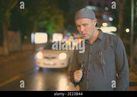 Reifer Mann rauchen Elektronische Zigarette in den Straßen bei Nacht Stockfoto