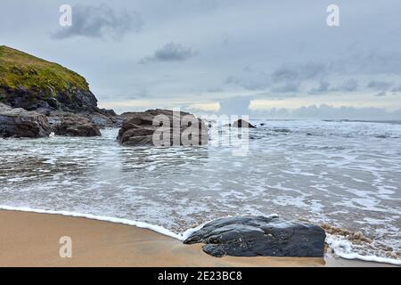 Bild von Poldhu Beach in Cornwall mit Felsen, Wellen, Sand und bewölktem Himmel. Stockfoto