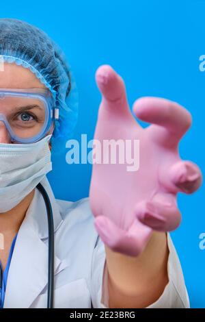 Ärztin streckt aus und will dich aus nächster Nähe greifen. Krankenschwesternhände mit roten bösen Augen greifen nach dem Patienten, blauer Hintergrund. Konzept des Aufenthalts zu Hause, Stockfoto