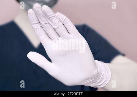 Der Arzt zeigt mit seiner Hand eine verbotende Geste der Füße, Nahaufnahme. Hand in einem medizinischen Handschuh mit einer Geste des Stopps, das Konzept der Bekämpfung t Stockfoto