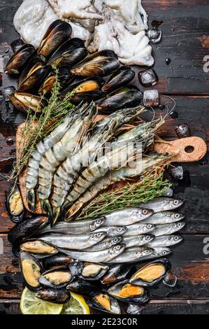 Verschiedene frische Meeresfrüchte Tigergarnelen, Garnelen, blaue Muscheln, Oktopusse, Sardinen, roch. Dunkler Holzboden Hintergrund. Draufsicht Stockfoto