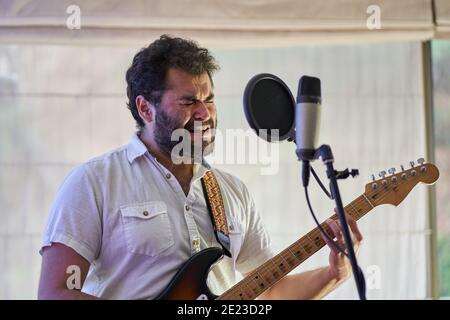 Emotionaler männlicher Musiker mit E-Gitarre, der begeistert singt und aufzeichnet In einem Studio Stockfoto