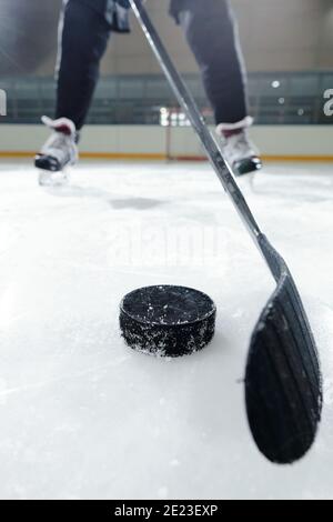 Beine des männlichen Hockeyspielers in Sportuniform und Schlittschuhe Stehen auf der Eisbahn gegen Stadion-Umgebung, während zu gehen Shoot Puck Stockfoto