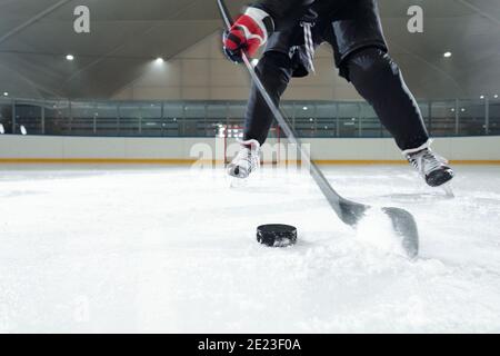 Hockeyspieler in Sportuniform, Handschuhe und Schlittschuhe, die sich vor der Kamera gegen die Stadion-Umgebung bewegen, während sie Puck schießen Stockfoto