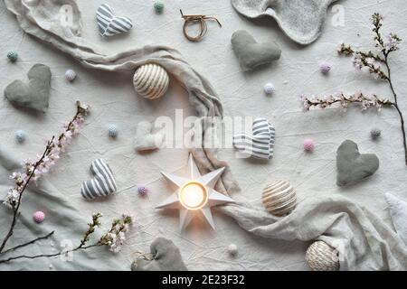 Handgemachte textile Herzen und Bälle auf Baumwollhintergrund. Textilhandwerk in neutralen Farben. Winterzeit Kirschblütenzweige und Kerze Stockfoto