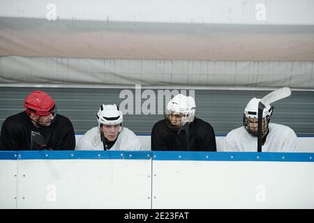 Gruppe von jungen Eishockeyspielern und ihre Trainer im Sport Uniform sitzen in Tribüne auf Stadion, während Pause oder Wiedergabe wird vorbereitet Stockfoto