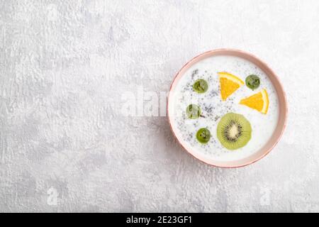 Joghurt mit Kiwi, Stachelbeere, Chia in Keramikschale auf grauem Betongrund. Draufsicht, flach liegend, Kopierraum. Stockfoto