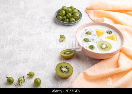 Joghurt mit Kiwi, Stachelbeere, Chia in Keramikschale auf grauem Betongrund und orangefarbenem Leinentextilien. Seitenansicht, Kopierbereich. Stockfoto