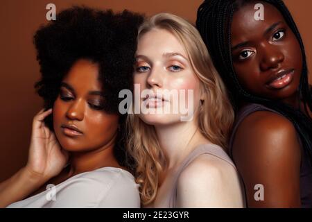 Junge hübsche kaukasische, afro, skandinavische Frau posiert fröhlich zusammen auf braunem Hintergrund, Lifestyle diverse Nationalität Menschen Konzept Stockfoto